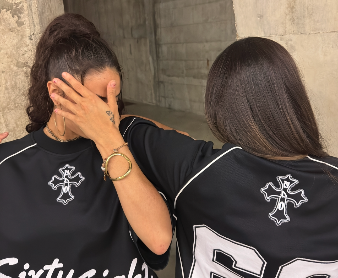 Two female models wearing the Studio Sixty Eight Jersey front and back. Showcasing the designs of the clothing. The letters, numbers and the cross design. With the streetwear style background. 